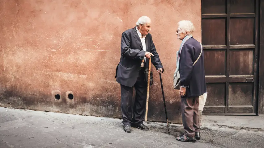 An elderly man and woman standing near a wall