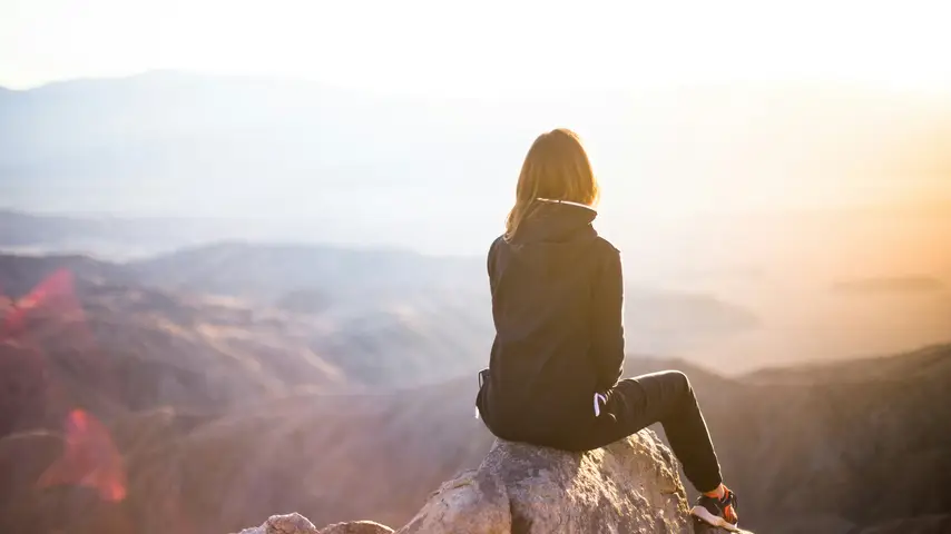 A woman sitting on top of a boulder overlooking mountains