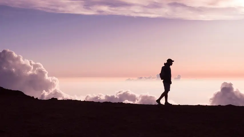 Silhouette of a person walking along a ridge with clouds in the background