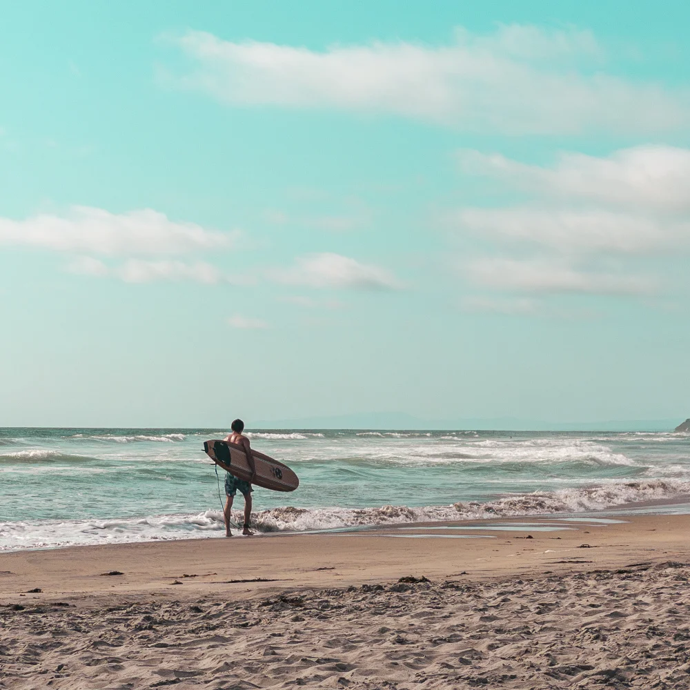 A man carrying a surfboard while walking along the beach in Del Mar, California