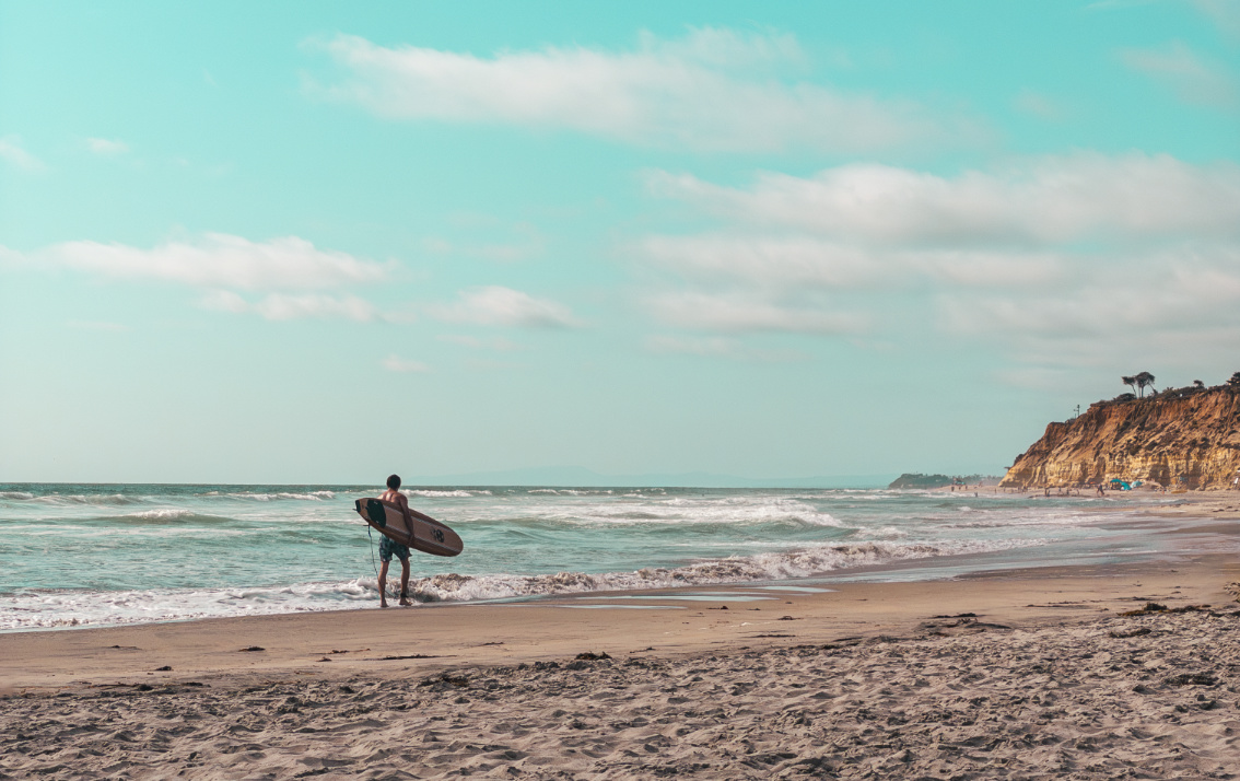 A man carrying a surfboard while walking along the beach in Del Mar, California